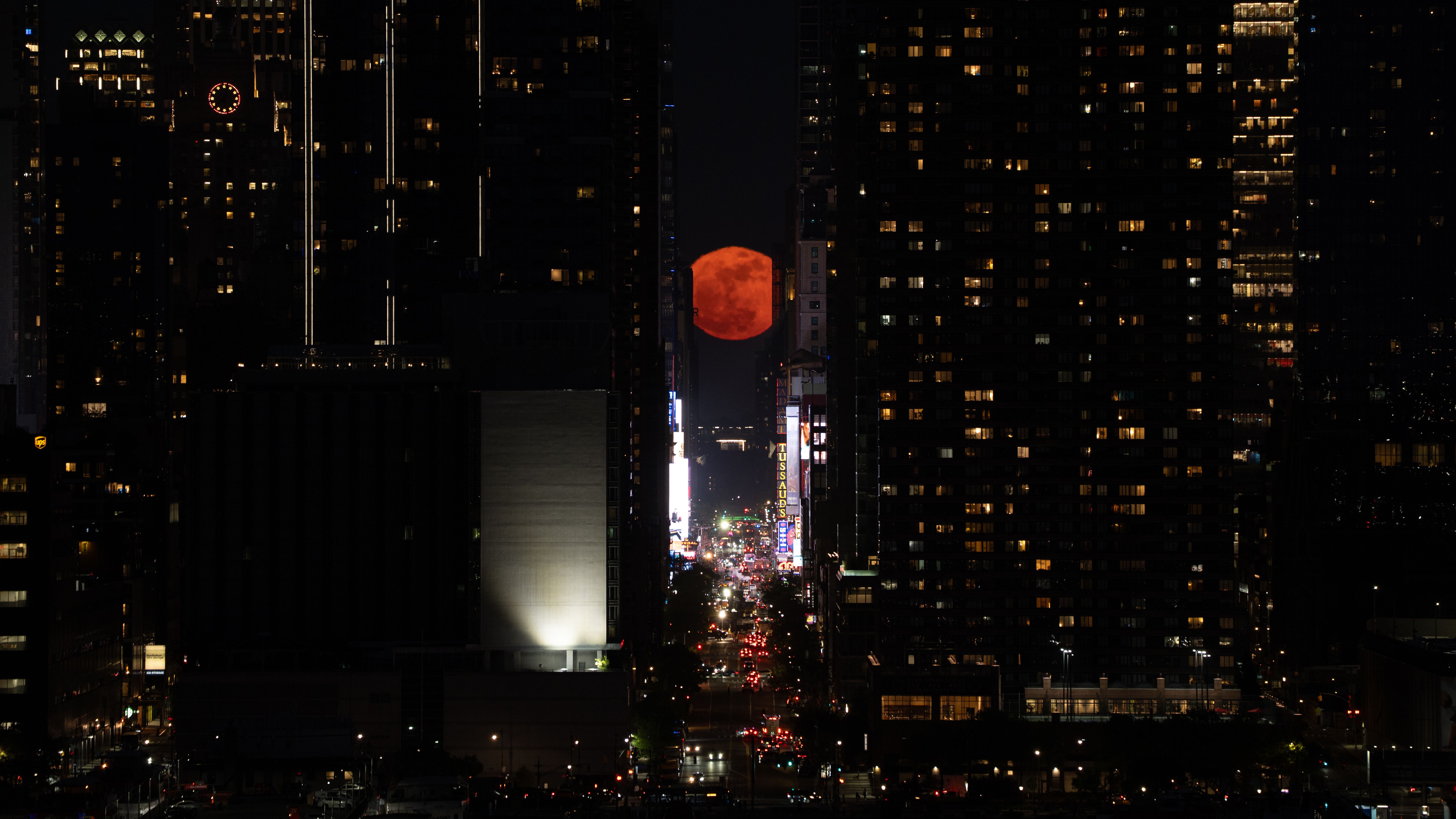 A red moon is pictured rising through 42nd Street in New York at night as traffic passes below.