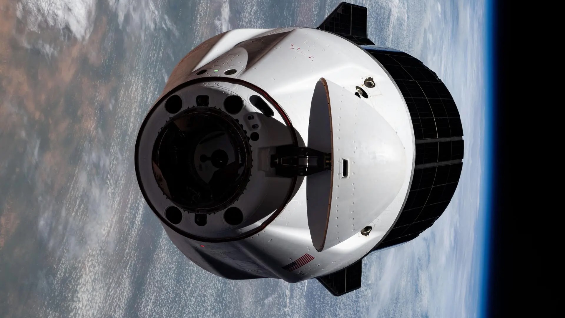 closeup photo of a white space capsule orbiting earth, with our planet in the background