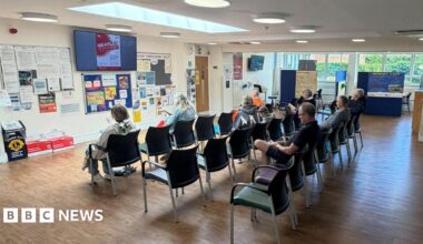 An image of the reception area at Oxted Health Centre. There are several rows of chairs with people sat in them.