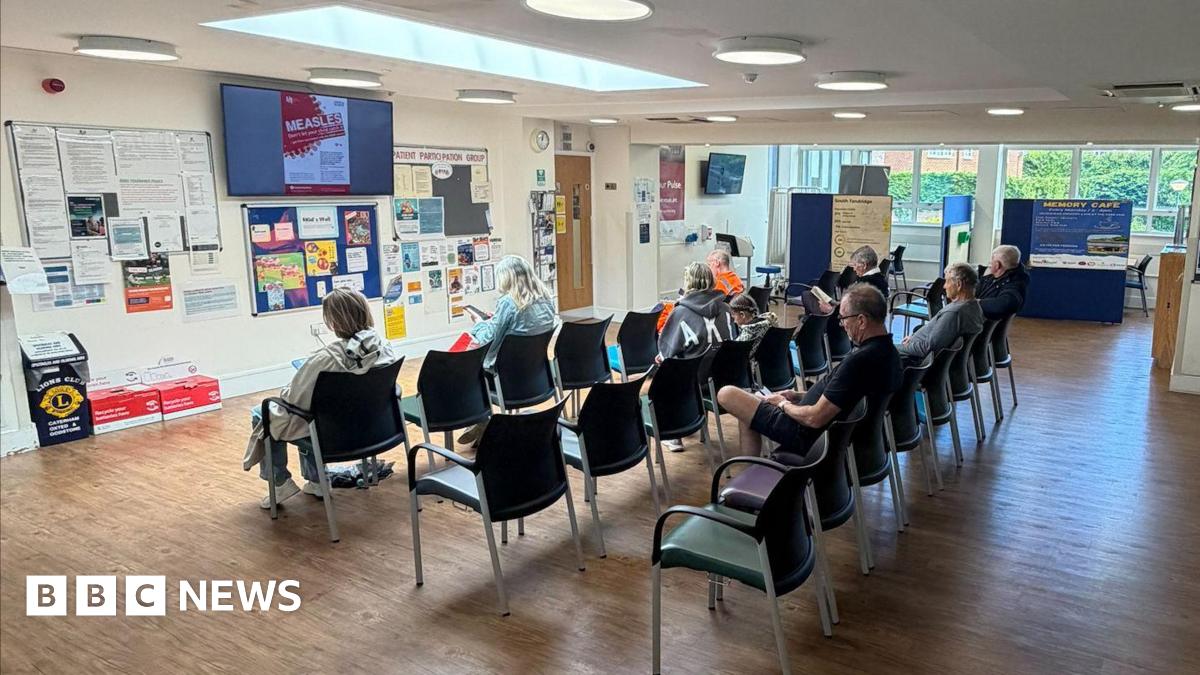An image of the reception area at Oxted Health Centre. There are several rows of chairs with people sat in them.