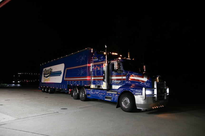 A massive blue, red and white truck is seen parked in a changeover station at night.
