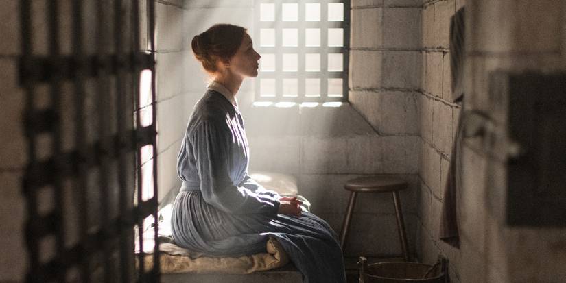 Grace Marks sitting on her cot in her prison cell facing the right stone wall, with sunlight streaming through the window onto her, in Alias Grace