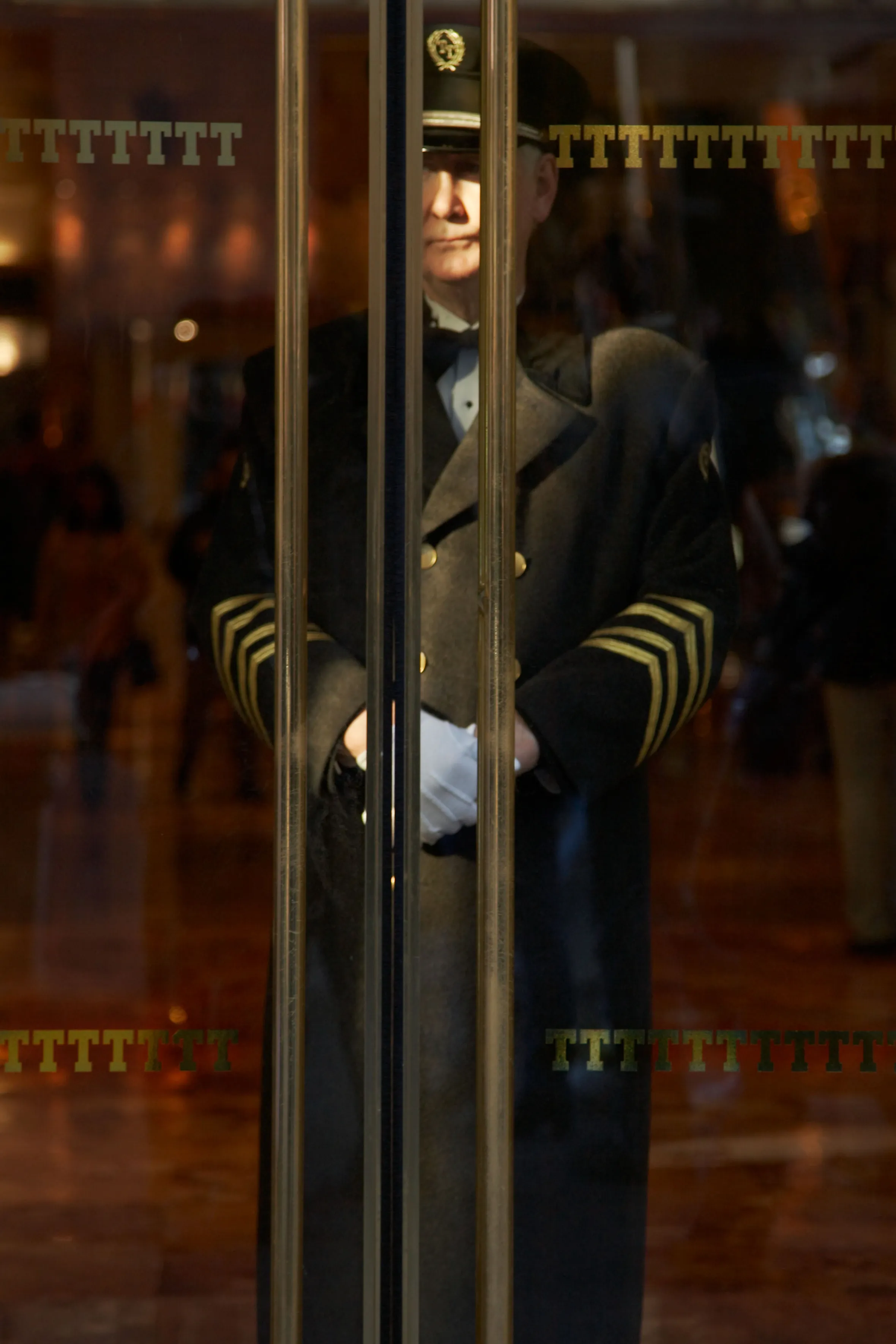 Doorman in uniform behind glass doors with the letters "TTTTTT" visible.