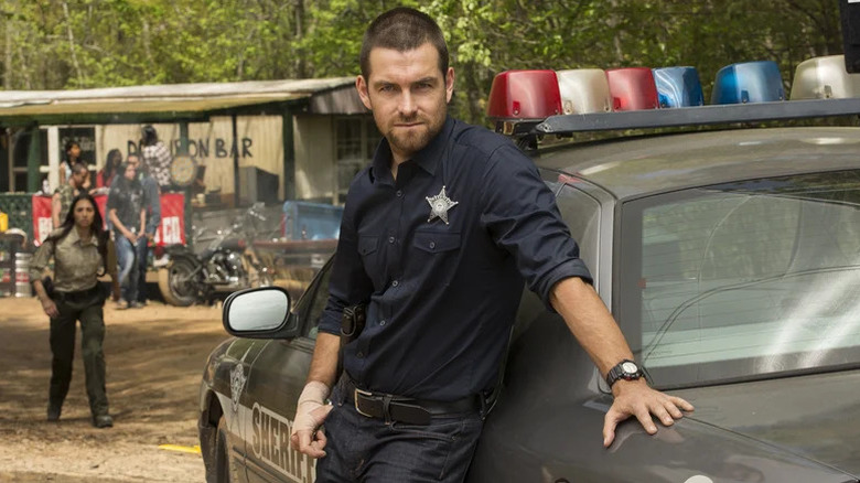 Lucas Hood leans against a sheriff's car in Banshee