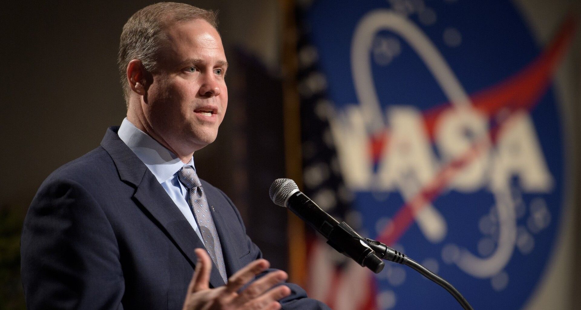 a white man in a suit talks into a microphone