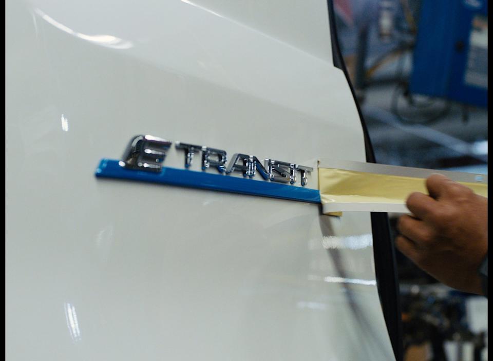 Person peeling tape off the logo on a Ford E Transit vehicle.