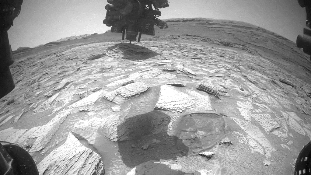 Looped video footage of a slab of rock stuck to the robotic arm of the Curiosity rover as the arm moves and rotates to remove it