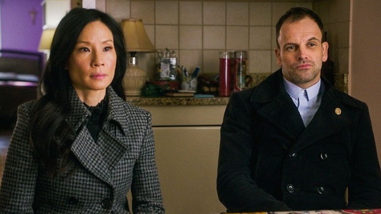 Lucy Liu as Joan Watson sitting next to Jonny Lee Miller as Sherlock Holmes in Elementary