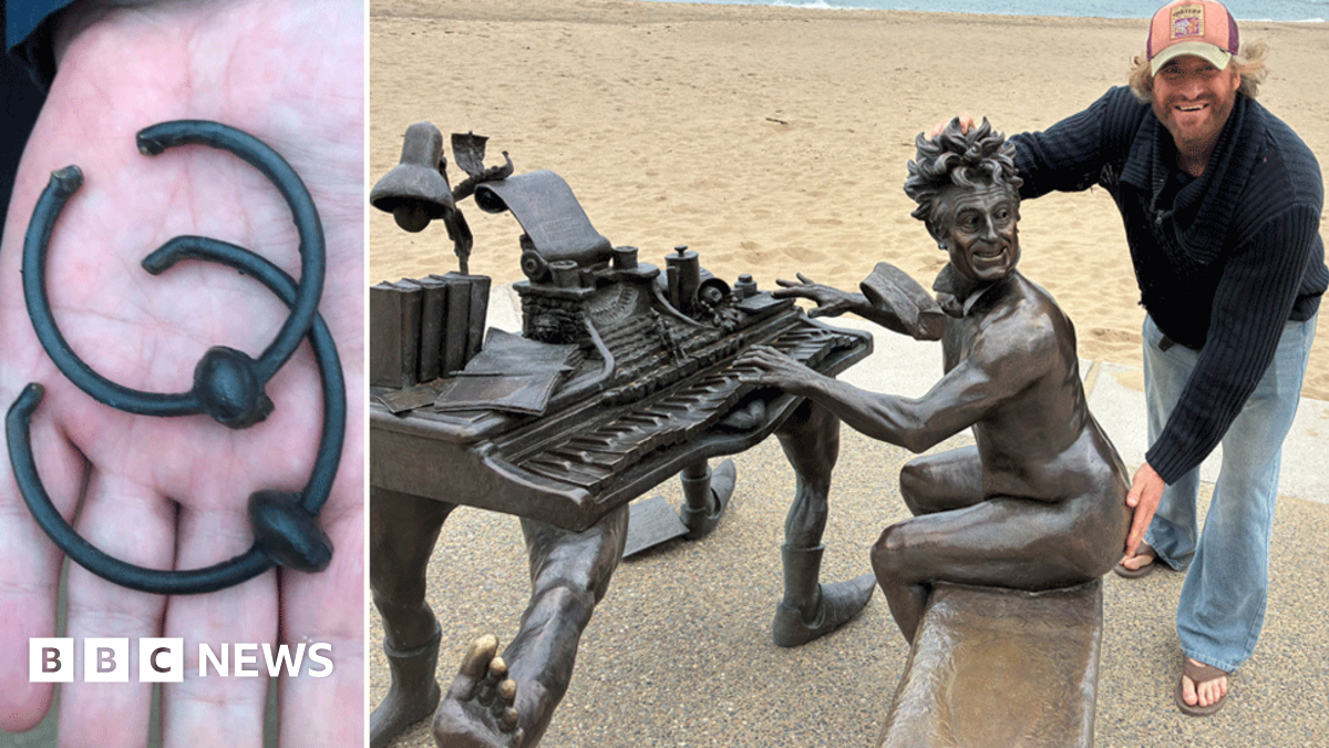 Crowd attends unveiling ceremony on a beach as two people pose for a photograph in front of statue of naked Terry Jones playing a piano
