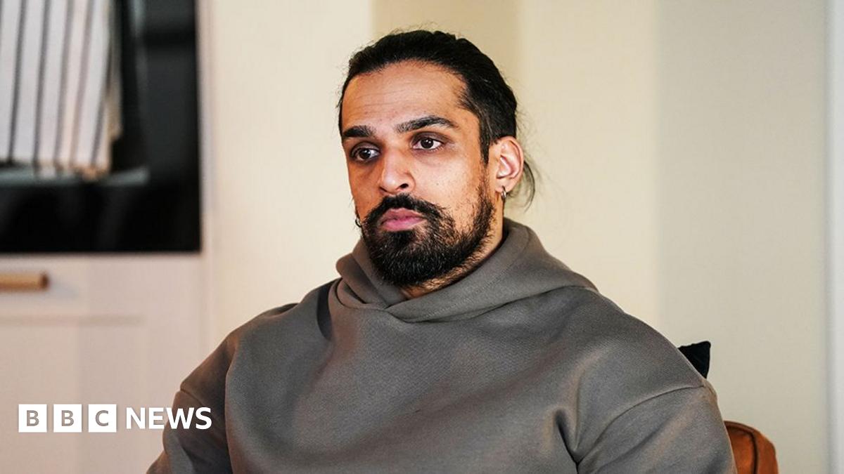 A still from EastEnders showing the character of Ravi, wearing a grey hoodie and looking into the distance.