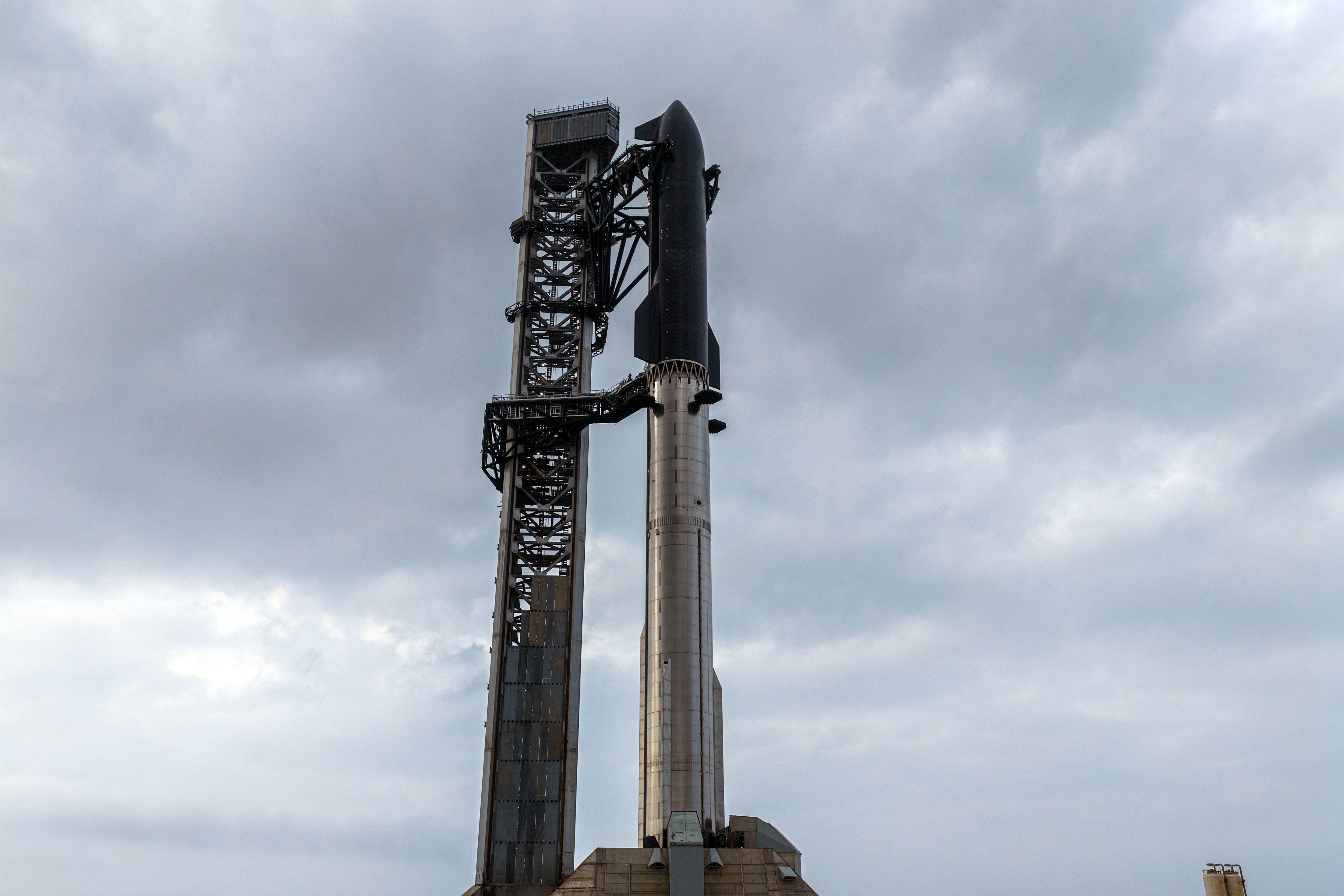 a giant chrome rocket booster and black-tiled spacecraft stand tall on a launchpad next to a gray tower.