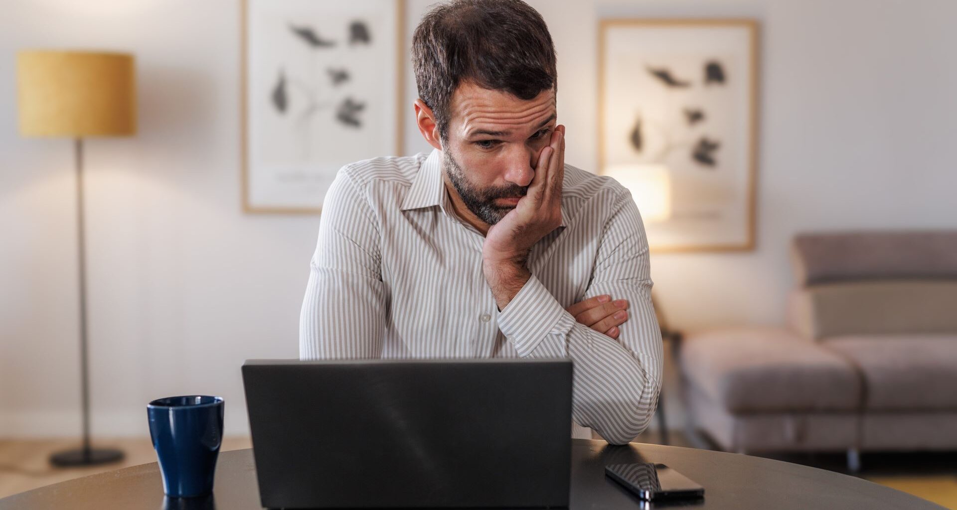A man looking at his laptop in a stressed and upset manner