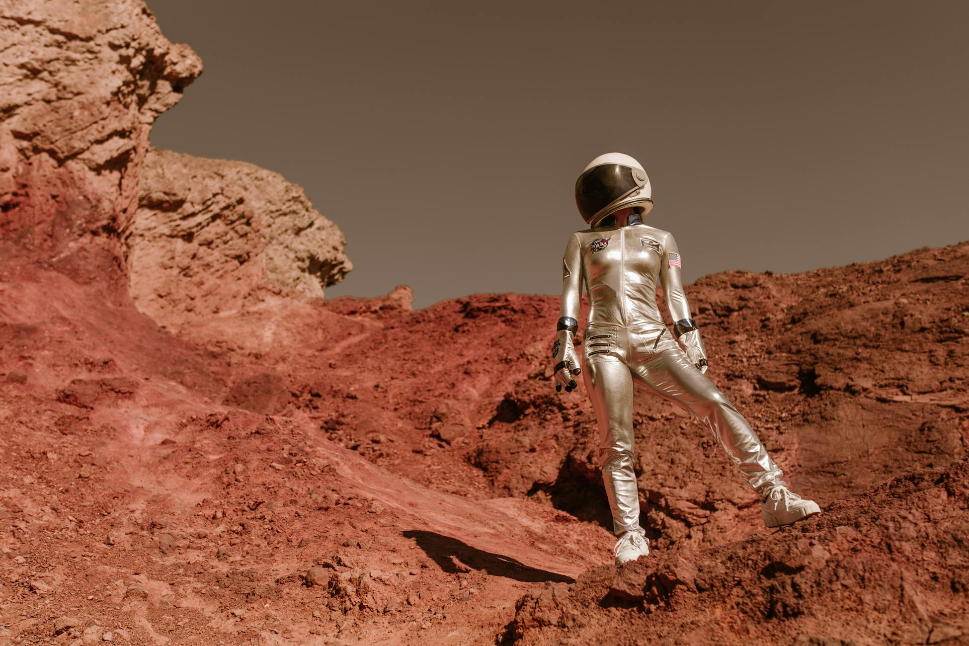 Astronaut in space suit standing on red rocky terrain resembling Mars' surface.