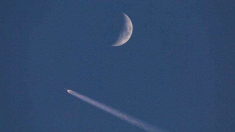 A SpaceX Falcon 9 rocket launches into Earth orbit against a waxing Moon in the background