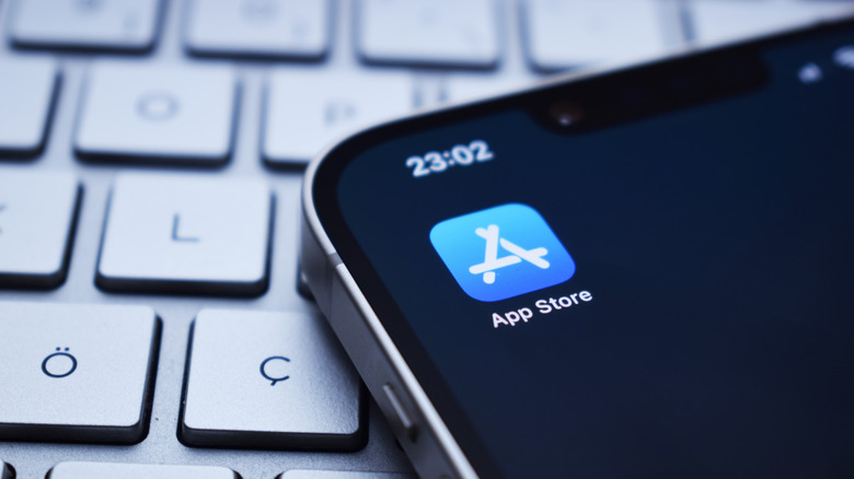 Close-up photo of an iPhone showing the App Store icon. The device is sitting on a wireless keyboard.