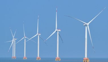 A series of white wind turbines sit in the ocean.