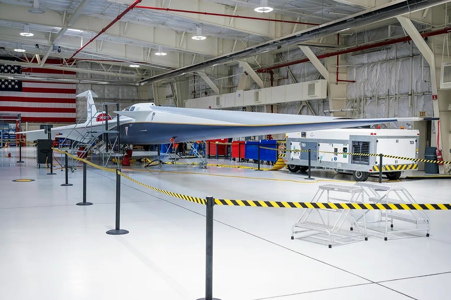NASA’s X-59 plane in a hangar with an American flag displayed behind it.