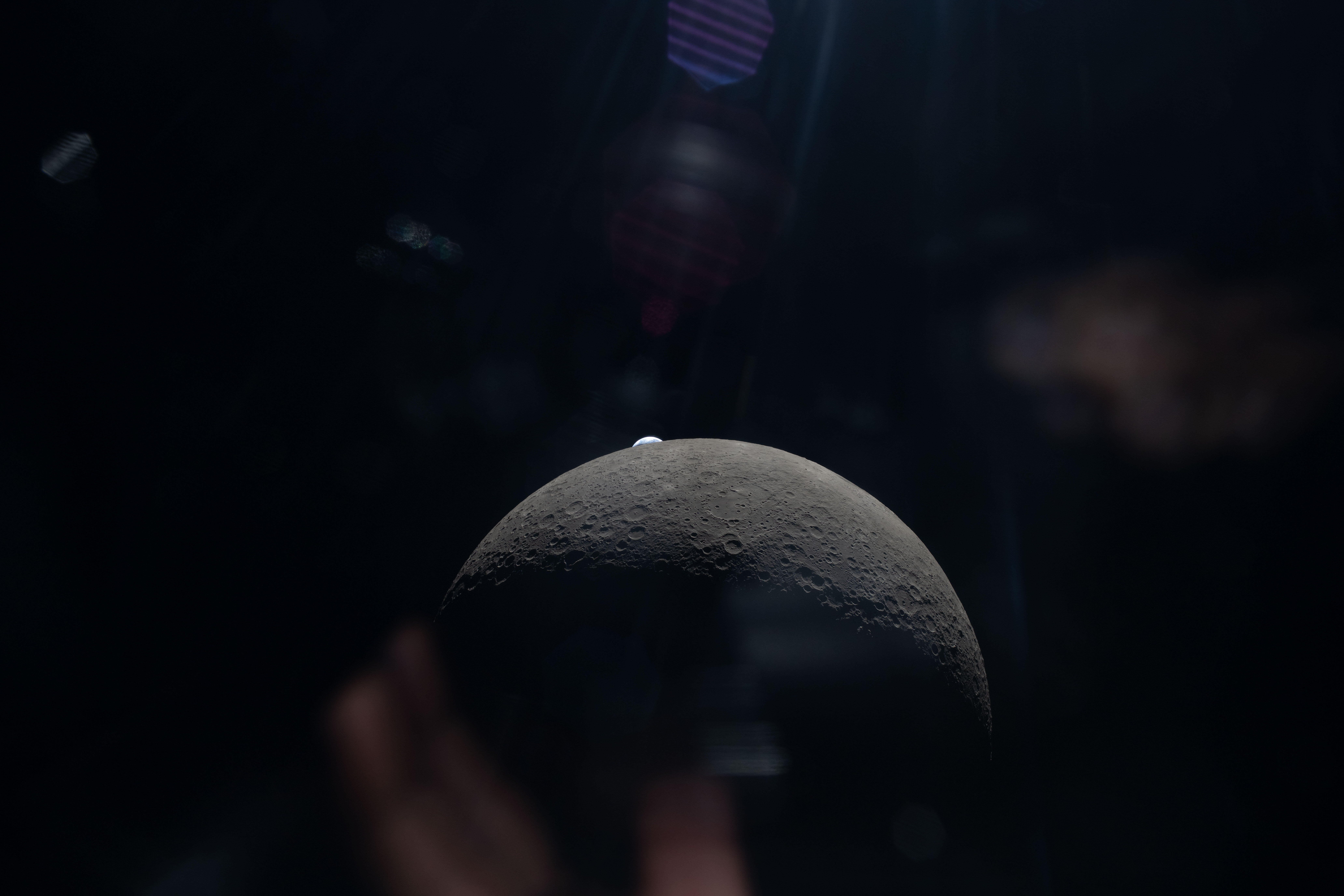 a tiny earth peaks up from behind a rising crescent moon