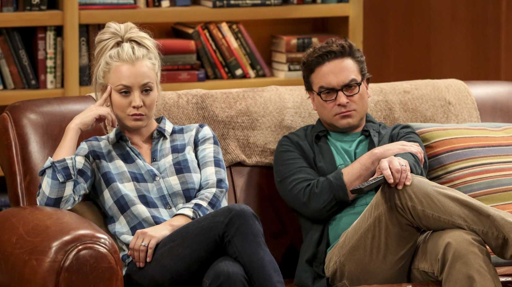 Penny (Kaley Cuoco) and Leonard (Johnny Galecki) sitting on the couch looking annoyed in The Big Bang Theory.