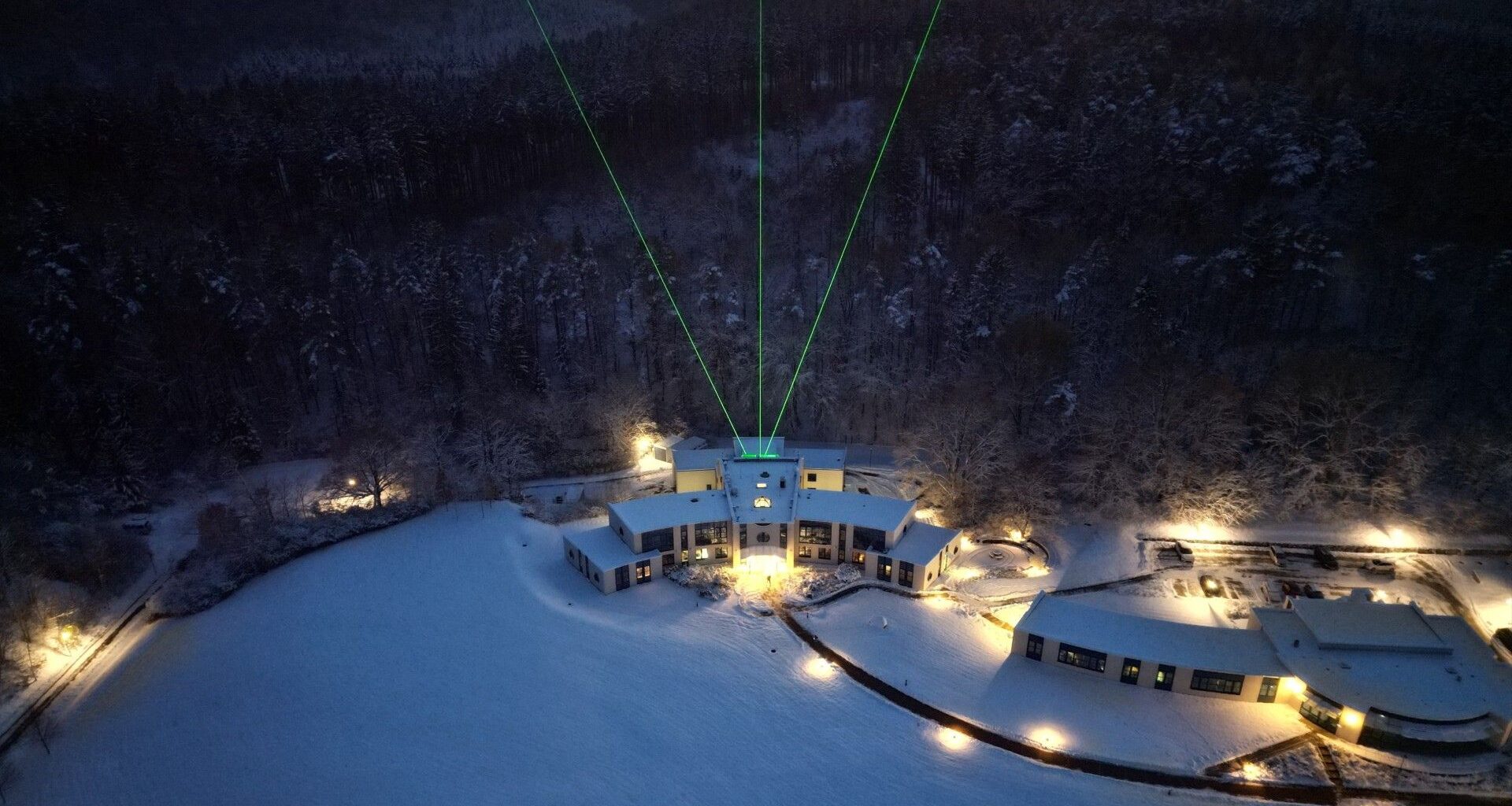 three green beams of light shoot skyward out of a building surrounded by a snowy alpine landscape