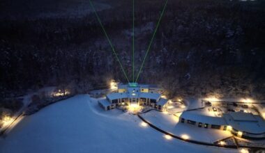 three green beams of light shoot skyward out of a building surrounded by a snowy alpine landscape