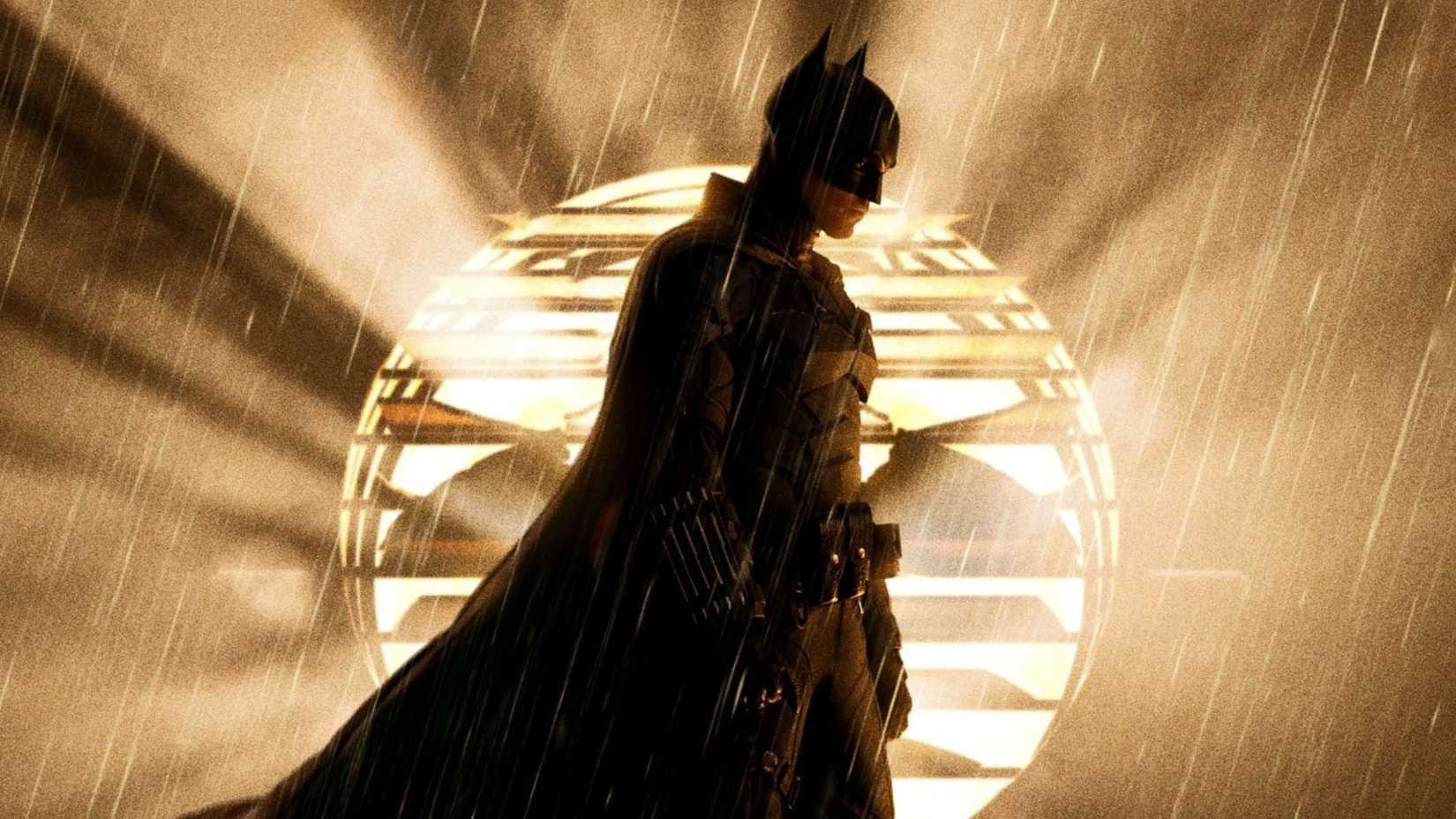 Robert Pattinson as Batman standing in front of the bat signal in The Batman