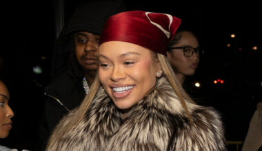 A woman with a red headscarf and fur coat smiles, surrounded by others in a dimly lit setting.