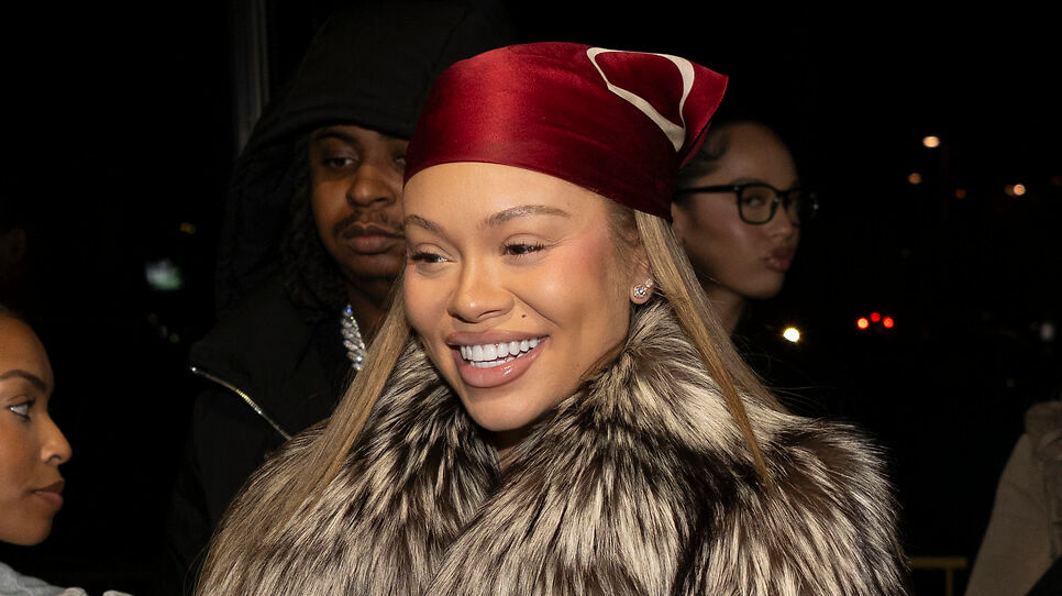 A woman with a red headscarf and fur coat smiles, surrounded by others in a dimly lit setting.