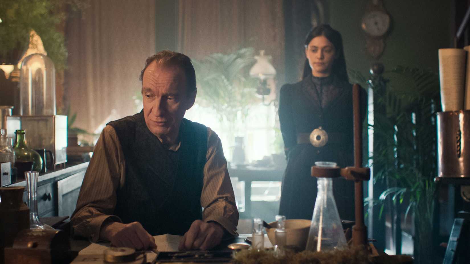A man at a desk and a woman in the background in the TV show Sherlock & Daughter.