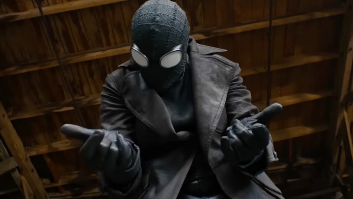 closeup of a man in black spiderman suit holding both hands out in front of him, ready to fire out webbing