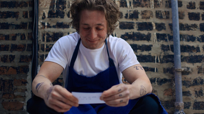 Carmy Berzatto smiling while reading a note in an alley