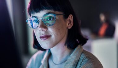 A person looking at data on a screen, with data reflecting in their reading glasses.