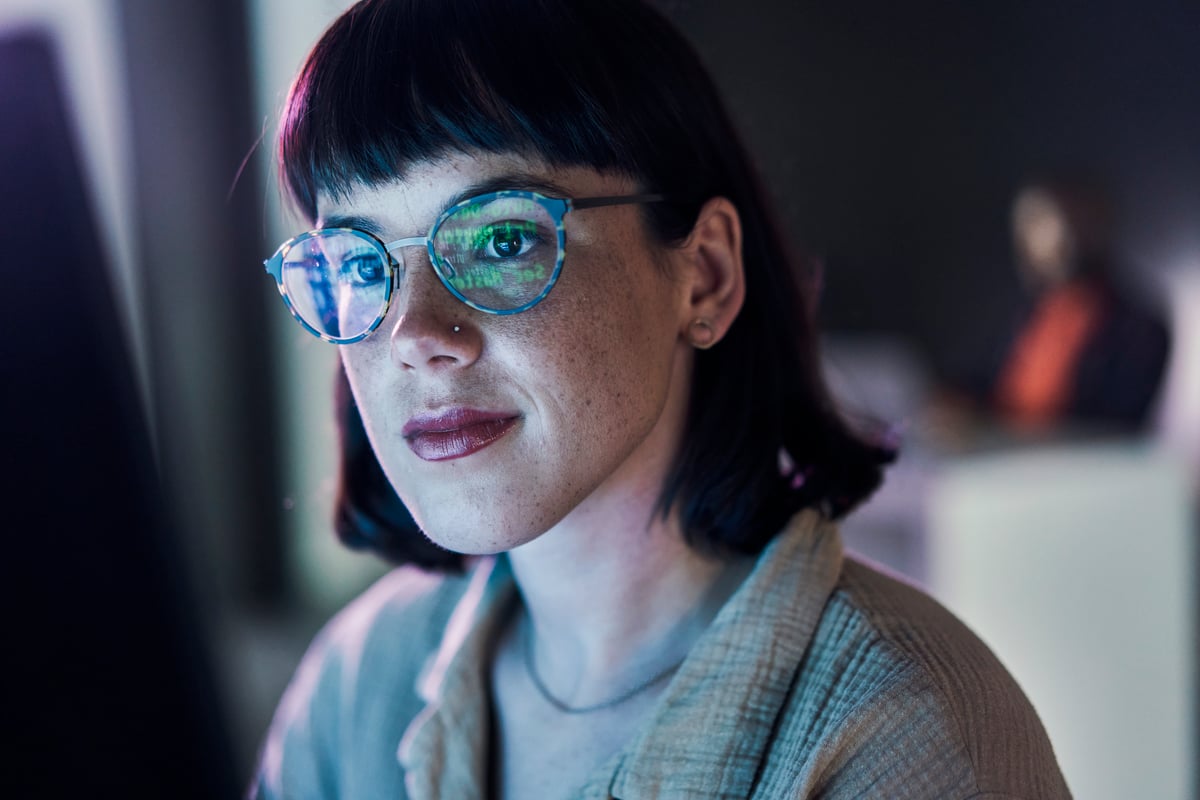A person looking at data on a screen, with data reflecting in their reading glasses.