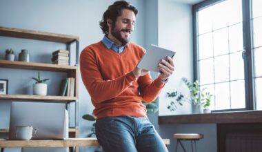 An investor leans against a desk and looks at something on a tablet.