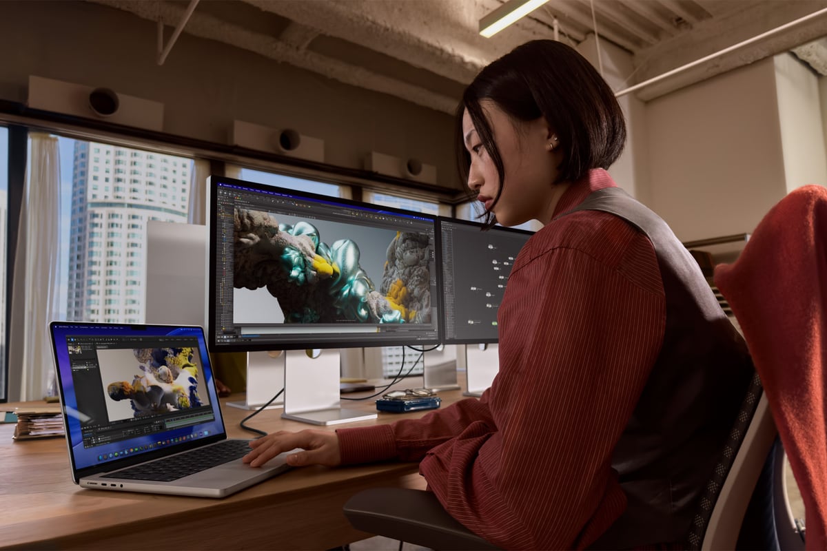 A woman working on a MacBook Pro, powering two high-resolution external displays.