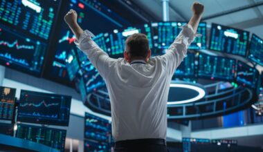 A person facing away from the viewer raises their fists in triumph as they watch a set of stock price monitors.
