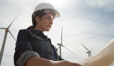 A person in work gear looking at blueprints with wind turbines in the background.