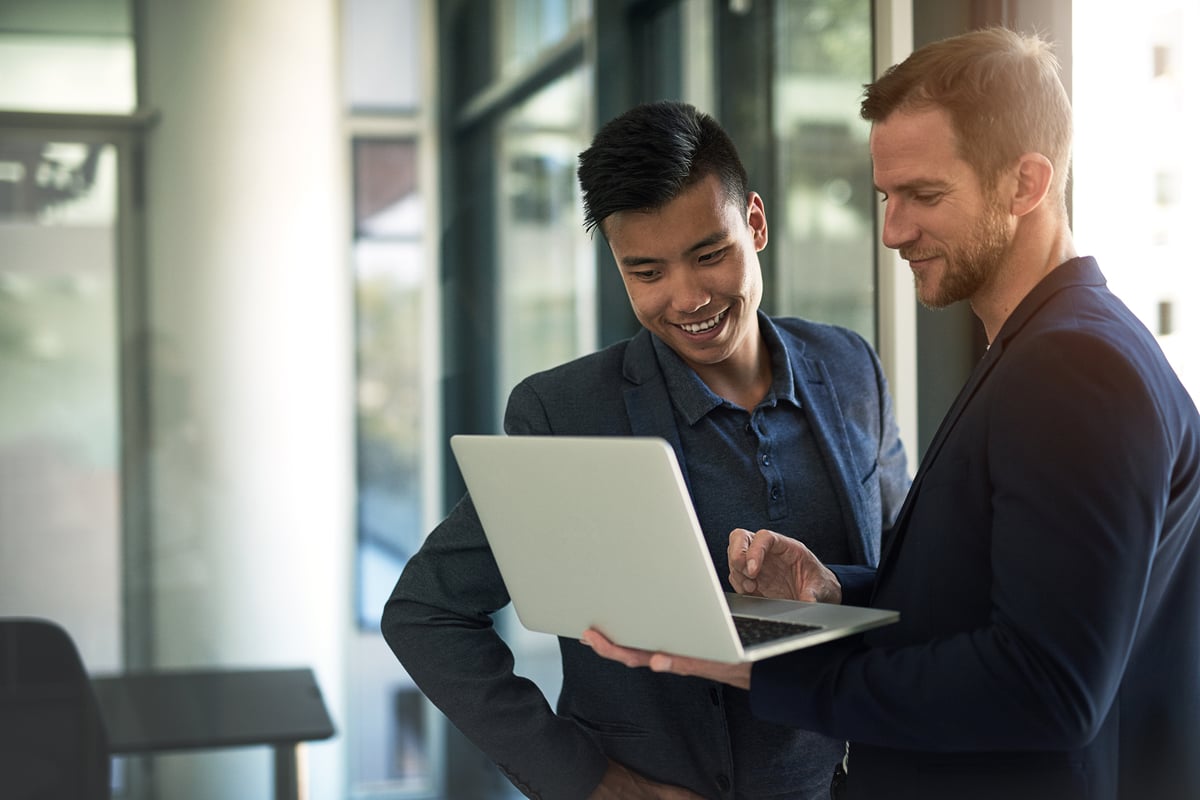 Two investors, standing in an office, look at something on a laptop.