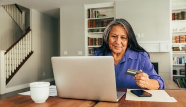 Smiling person holding debit card and typing on laptop.