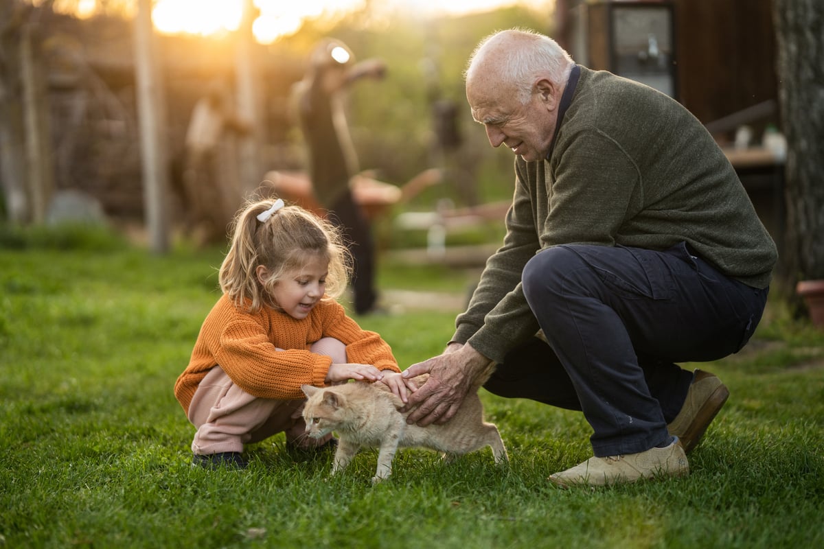 Senior and child petting cat in backyard.