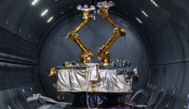 a cube-shaped satellite with two multi-jointed arms inside a cleanroom