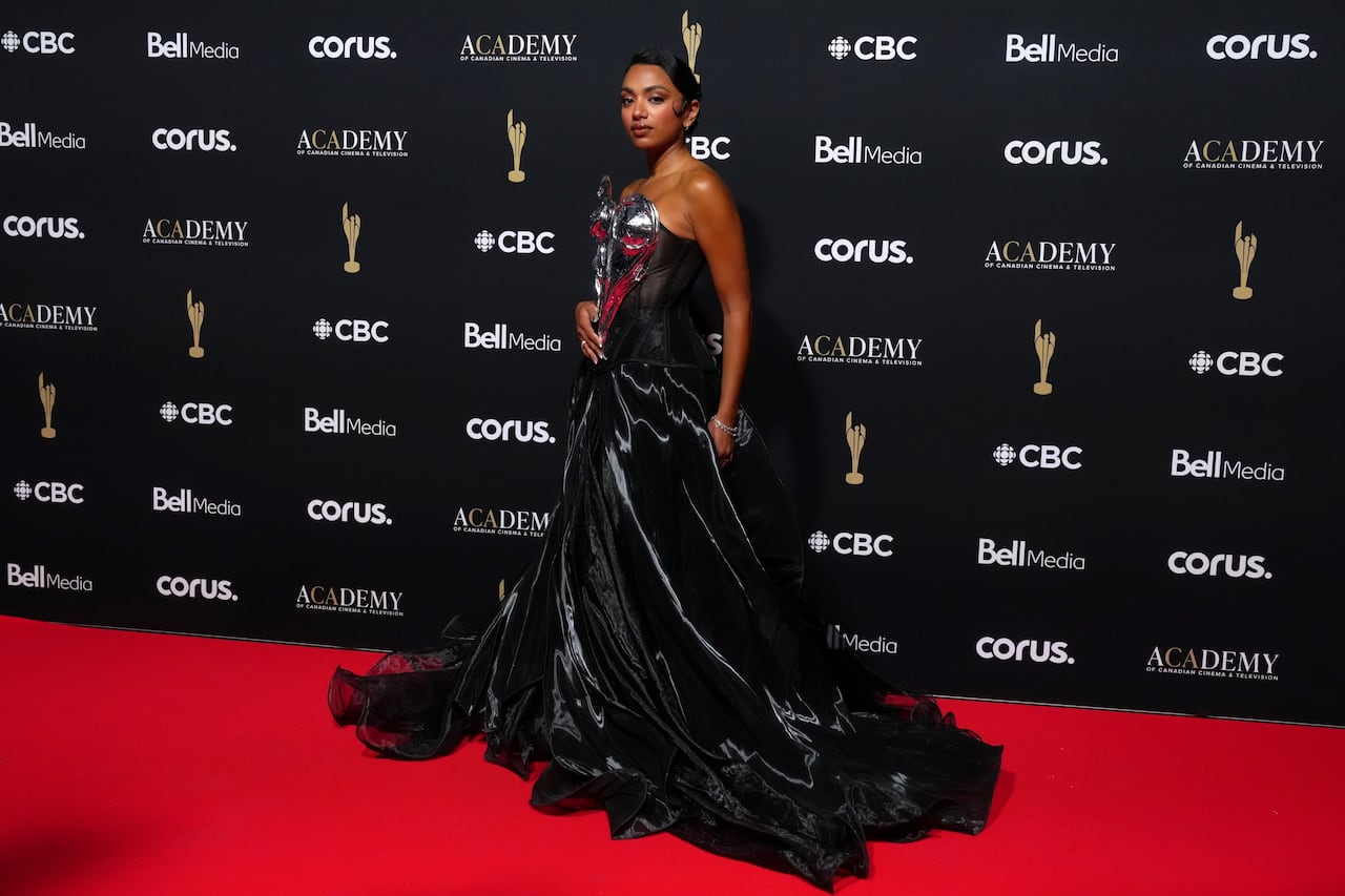 A woman poses for a photo in a black strapless gown with silver and red details on the corset.