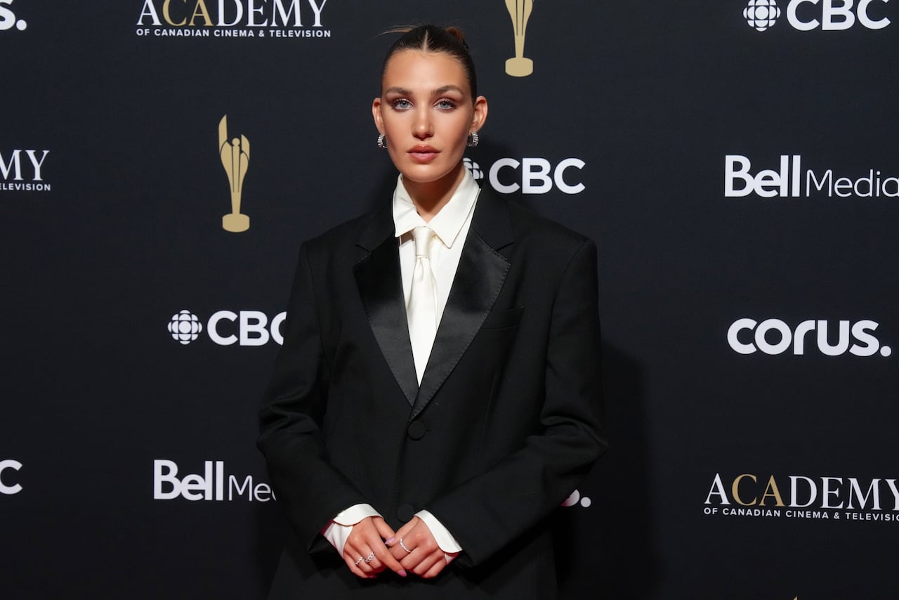 A woman poses for a photo wearing a black suit with white shirt and white tie.