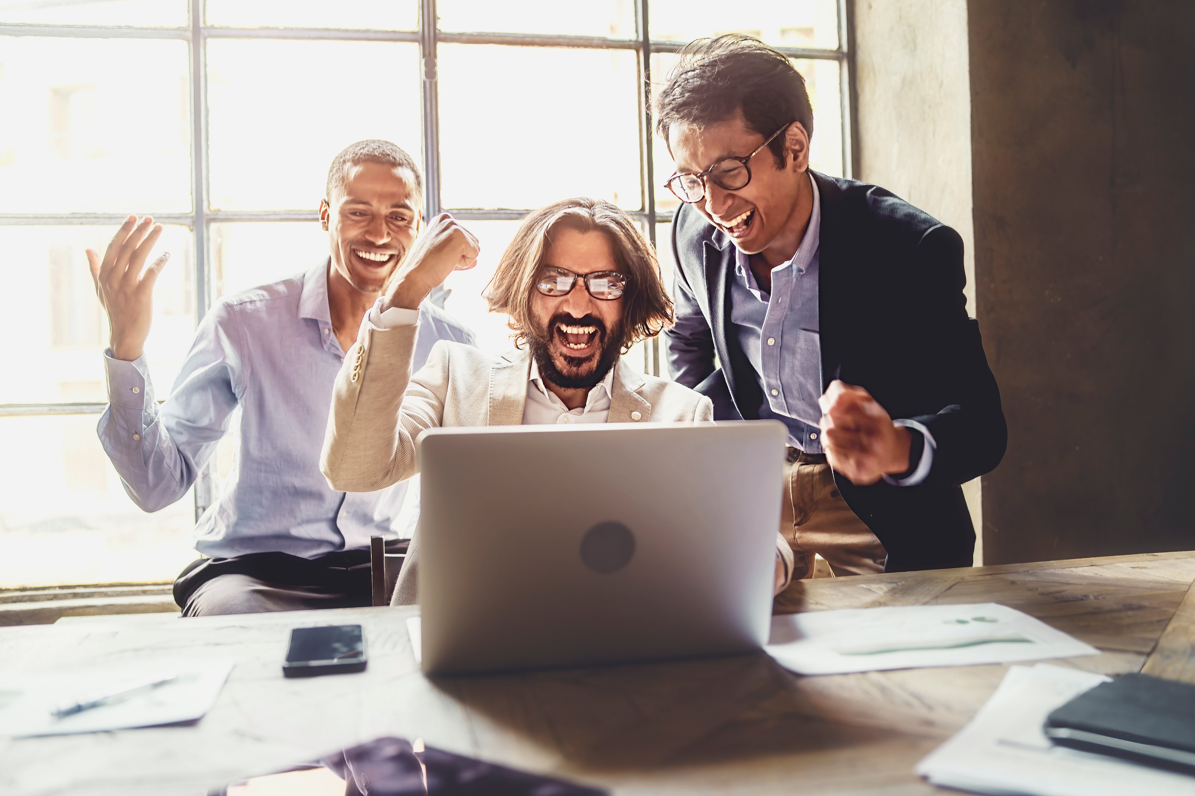 Three people looking at laptop and celebrating.