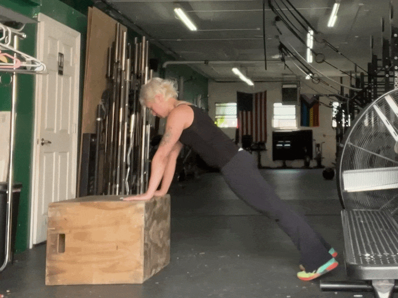 This is a photographic GIF showing a close-up of an inclined pushup exercise. In this exercise, place your hands on an elevated surface like a counter or bench, and plank your body in a straight line from your head to your heels. Bend your elbows to lower your chest, and then press back up.