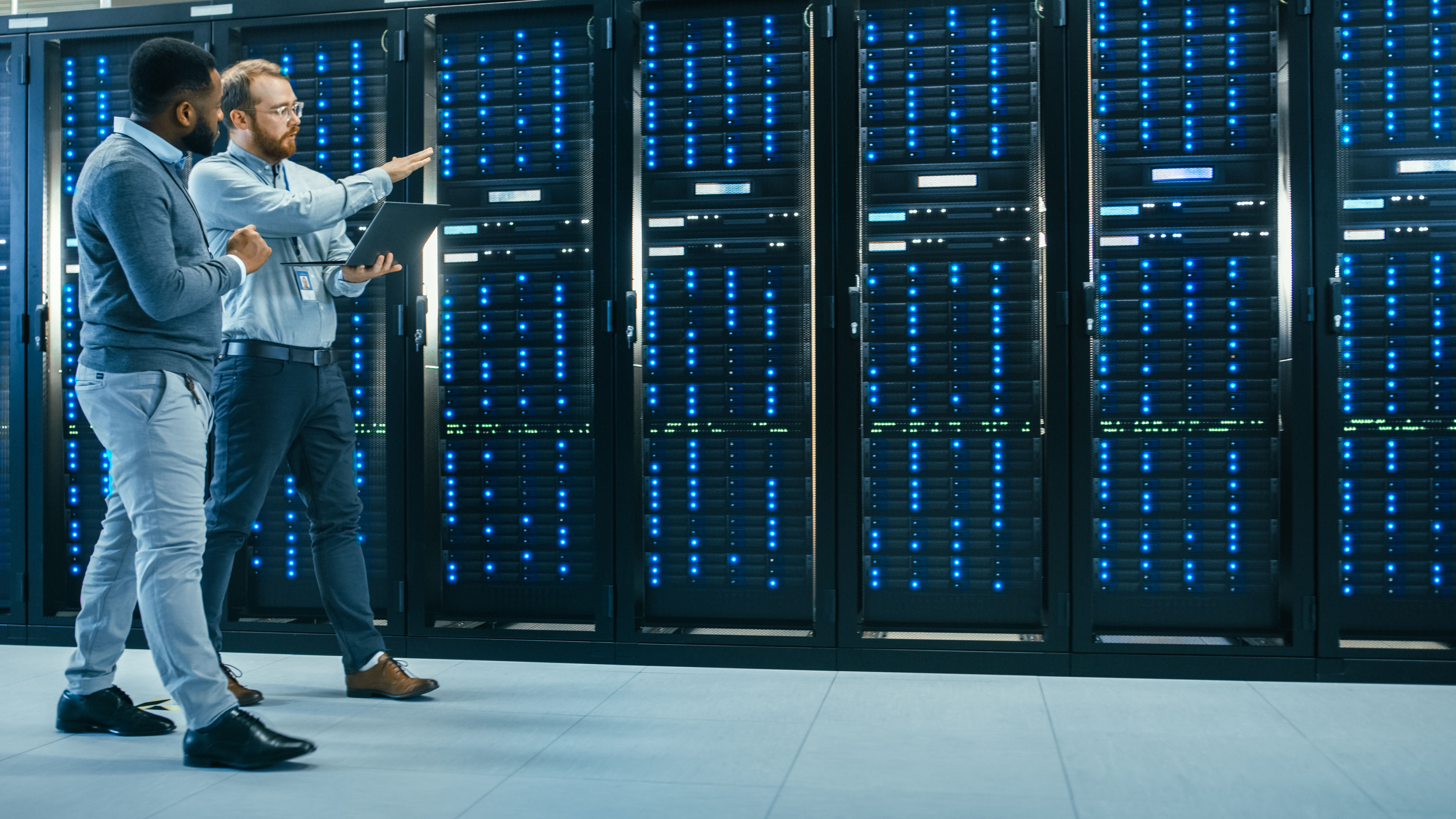 Two AI data center technicians are walking through a row of data center racks.
