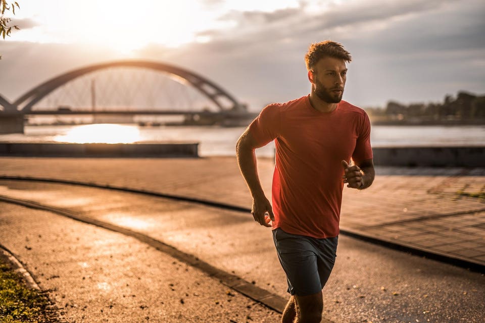 An athletic male CEO running outdoors in the city at sunrise before his business meetings.