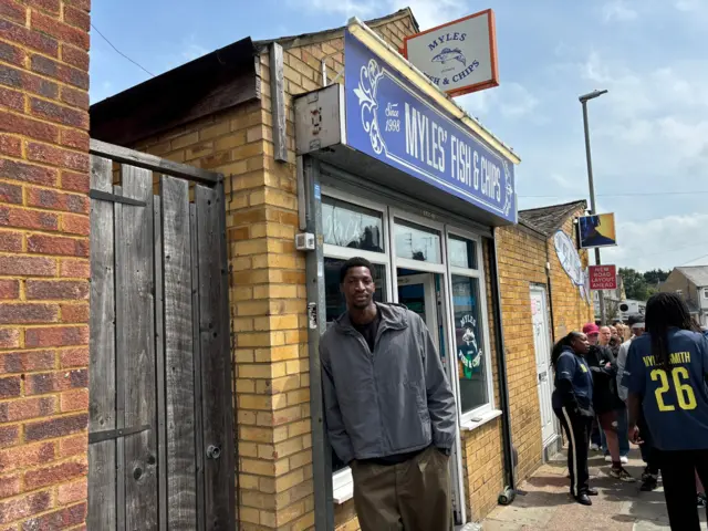 A man standing outside a fish and chip shop called Myles Fish & Chips