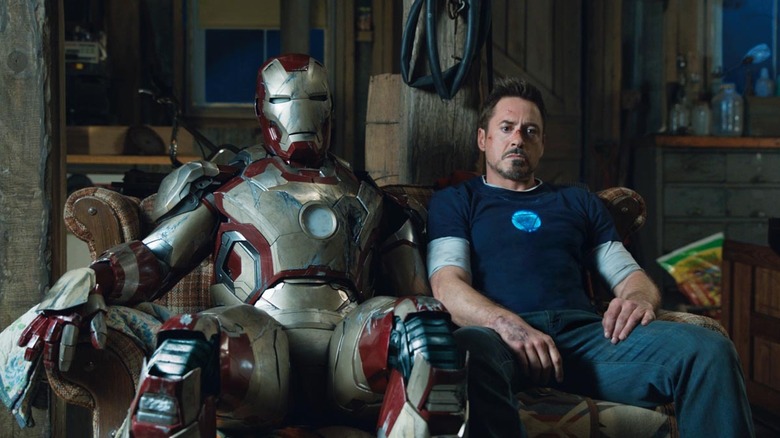 Robert Downey Jr. as Tony Stark, sitting with an Iron Man in Iron Man 3.