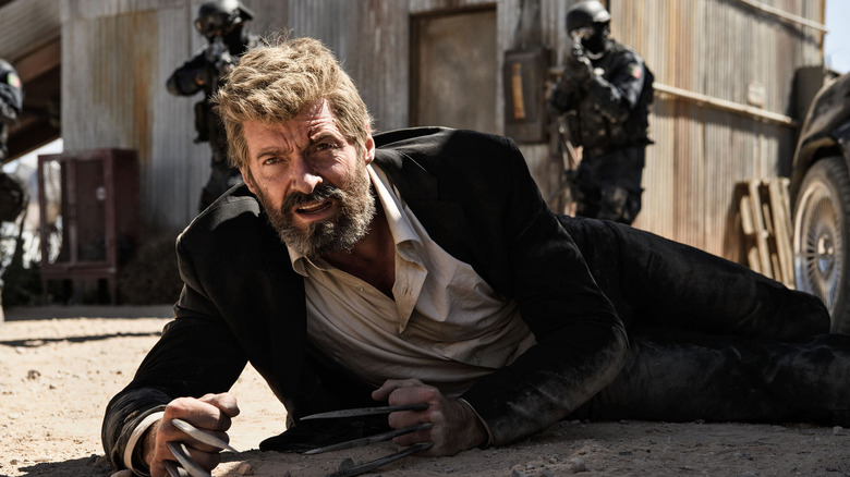 Logan lies on the ground with his claws out, surrounded by armed soldiers in Logan.
